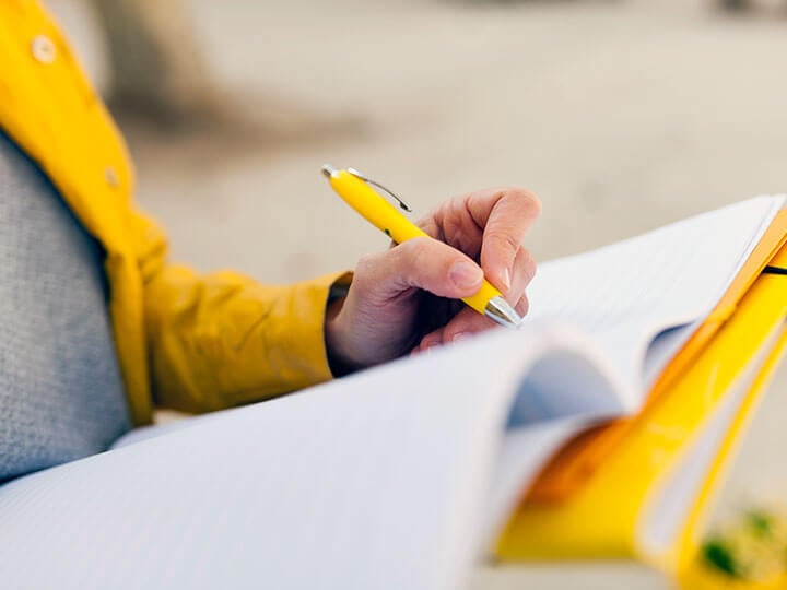 close up of a person in yellow jacket writing on a clipboard